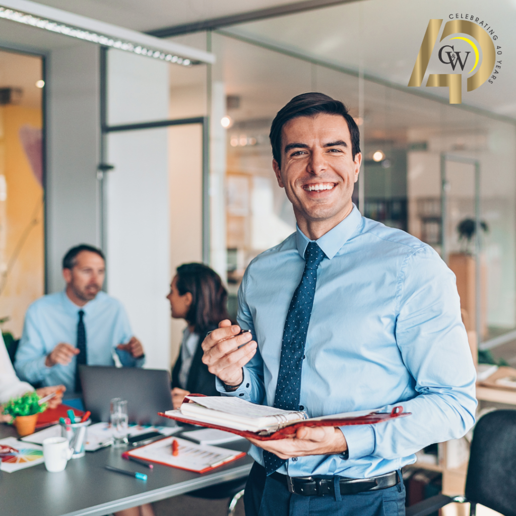 Businessman smiling at camera while two individuals behind him discuss Managed IT Services in Florida